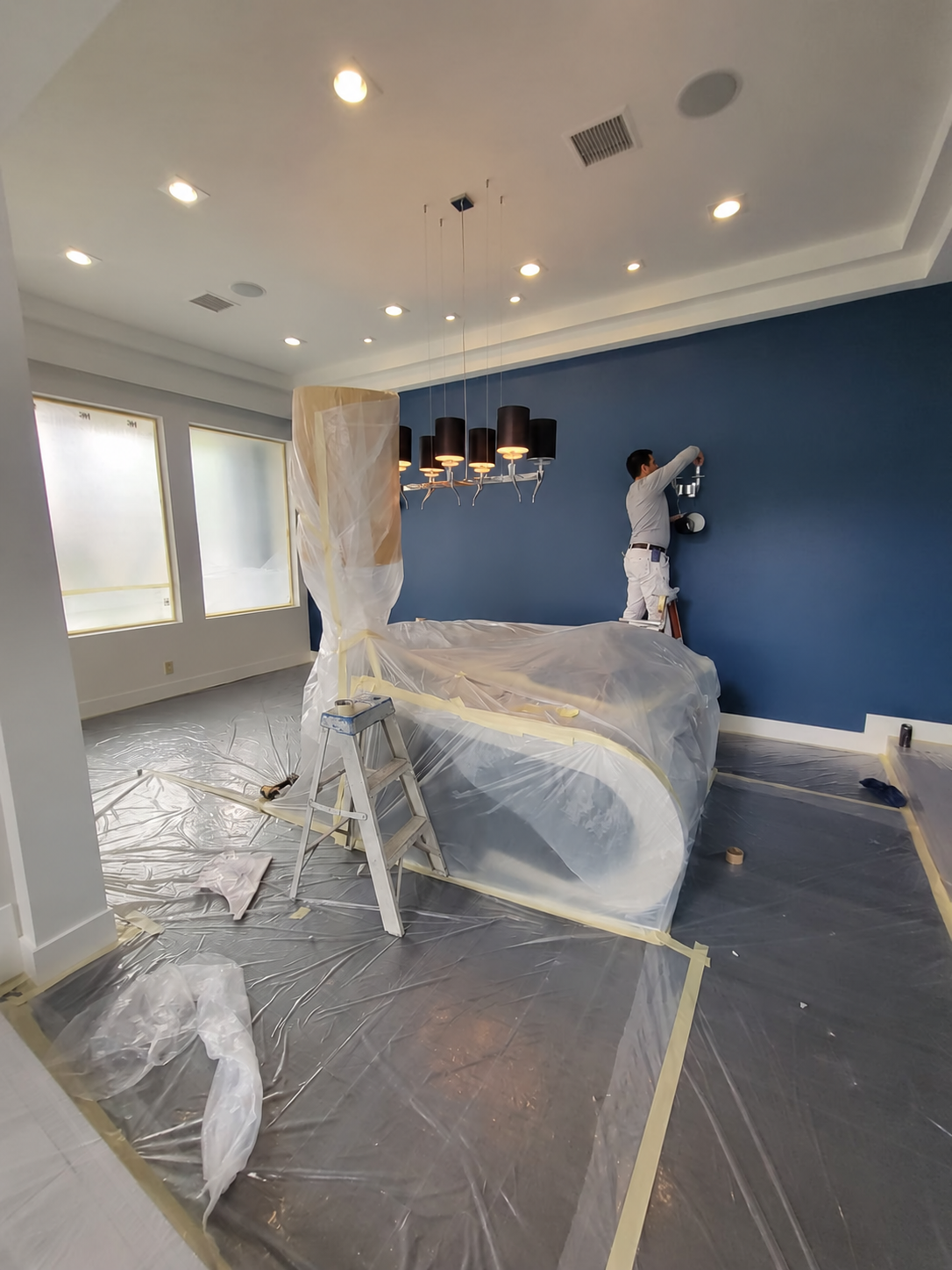 Painter applying interior wall paint in a room with protected furniture and floors